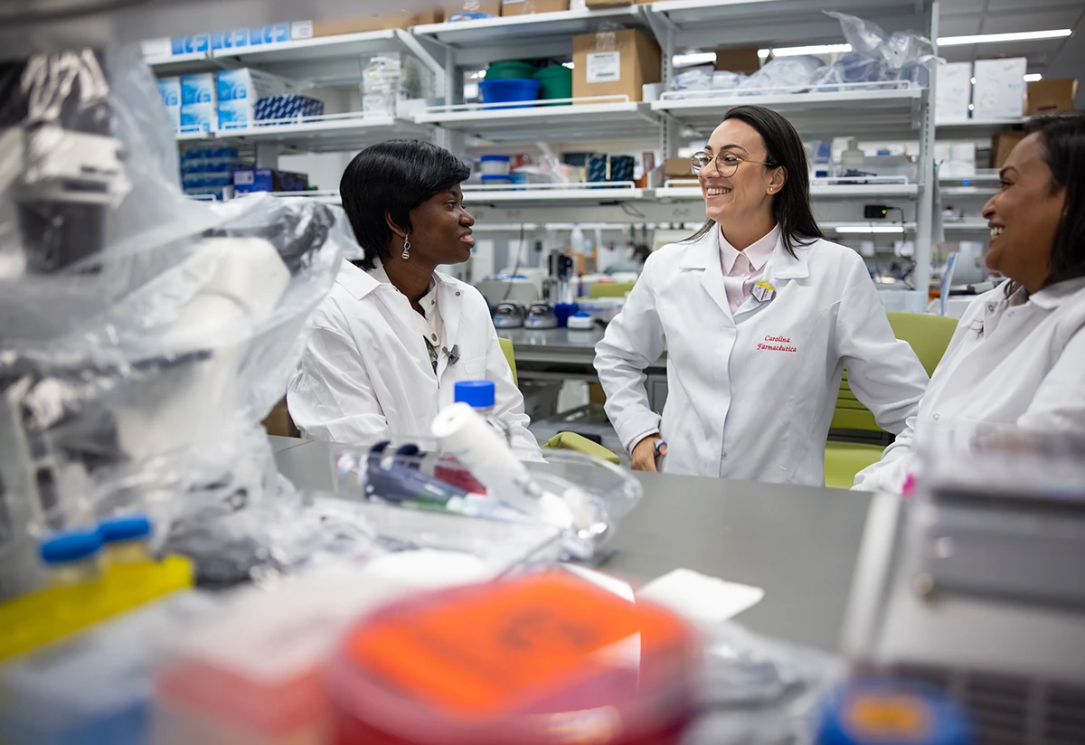 Two students and researcher Carolina Ferreira in lab coats having a conversation in a laboratory