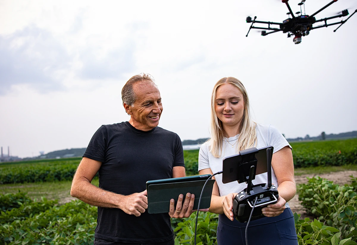 Researcher Bruno Basso and a student stand in a crop field while a drone hovers nearby